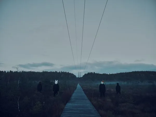 Band photo. The four band members stand in a mist covered mire wearing black clothes and animal masks, resembling from left to right a bear, a rabbit, a cat and a crow. Between the rabbit and crow there is a wooden bridge leading towards the horizon and above are high voltage powerlines leading in the same direction.